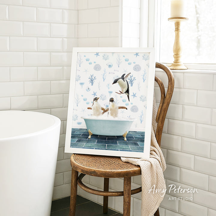 A framed image of two penguins sitting in a bathtub, surrounded by various marine life, is displayed on a wooden chair in a bathroom setting.