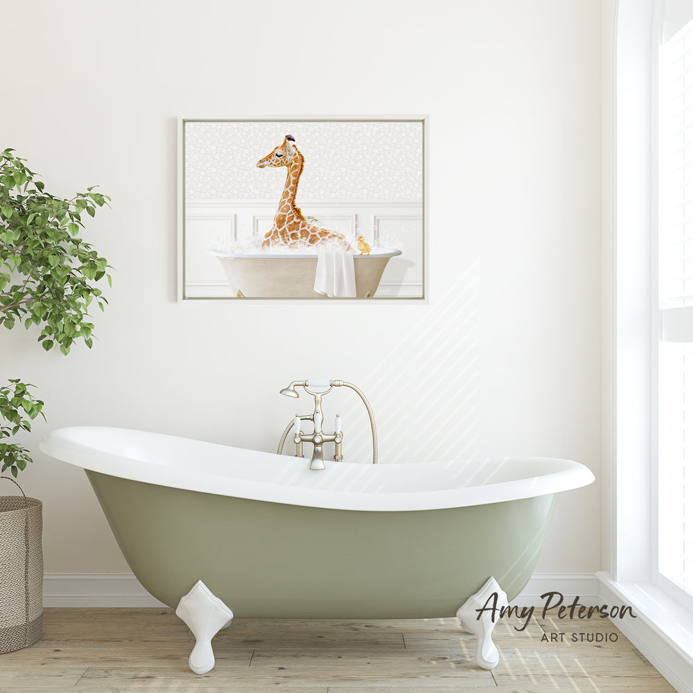 A framed image of a giraffe sitting in a bathtub is displayed on the wall above a green clawfoot bathtub in a bright, white-walled bathroom.