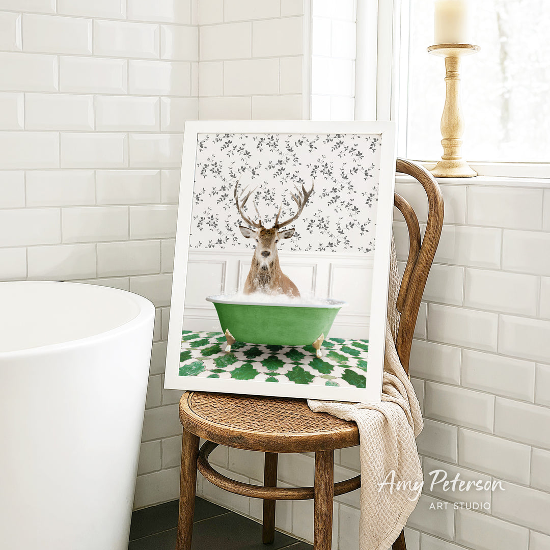 A framed image of a deer sitting in a green bathtub, surrounded by a floral pattern, is displayed on a wooden chair in a bathroom setting.