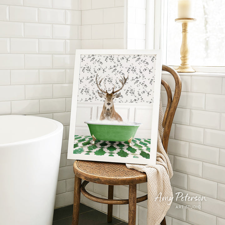 A framed image of a deer sitting in a green bathtub, surrounded by a floral pattern, is displayed on a wooden chair in a bathroom setting.