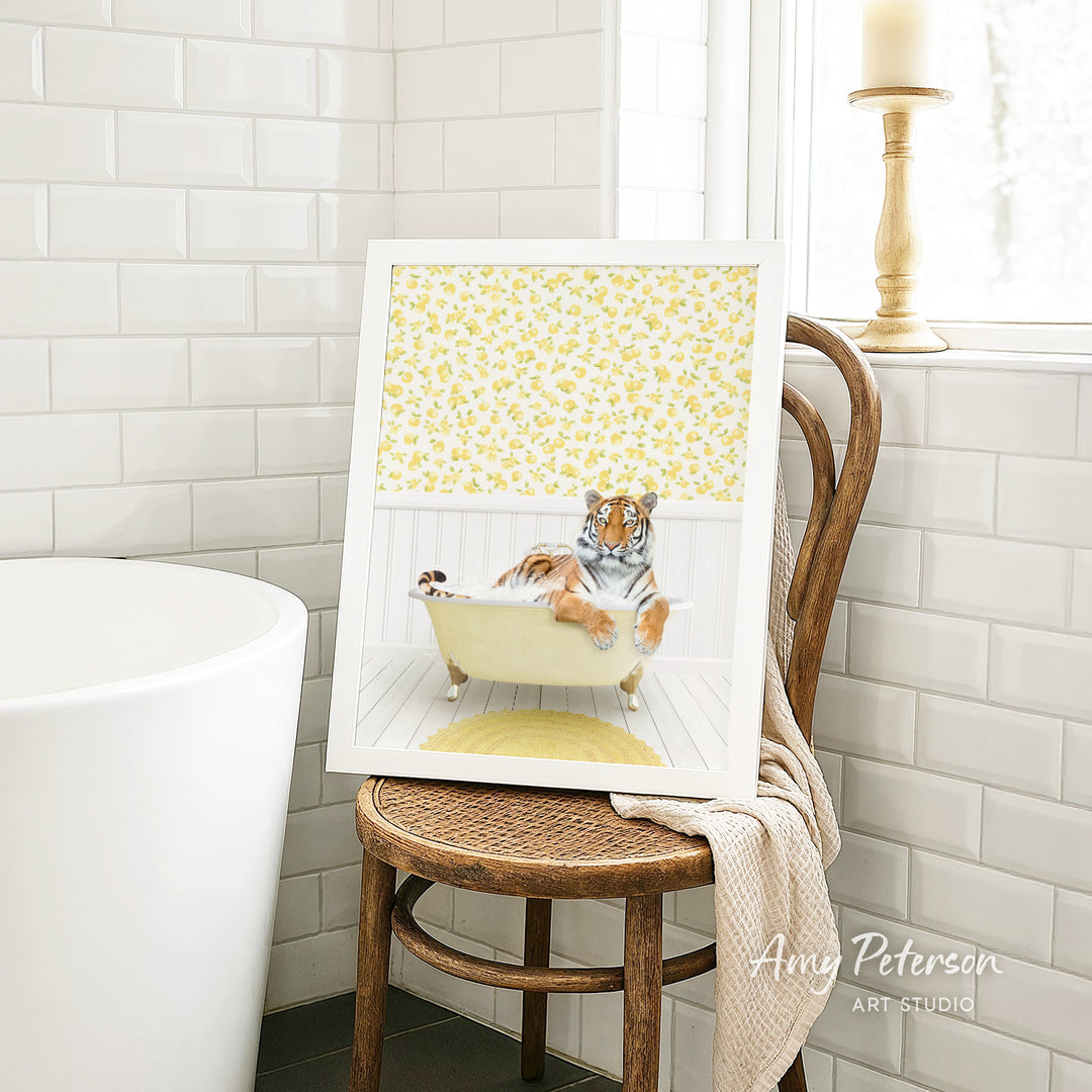 A framed image of a tiger sitting in a bathtub, surrounded by yellow flowers, is displayed on a wooden chair in a bathroom setting.