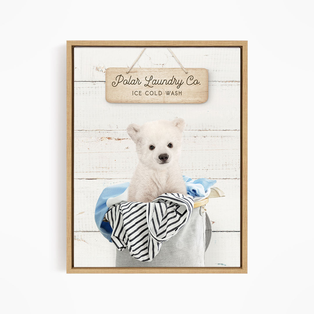 A white dog sitting in a laundry basket filled with clothes, with a wooden sign above that reads "Polar Laundry Co. Ice Cold Wash".