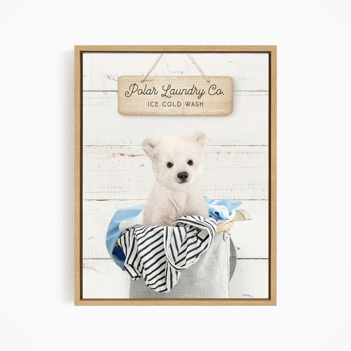 A white dog sitting in a laundry basket filled with clothes, with a wooden sign above that reads "Polar Laundry Co. Ice Cold Wash".