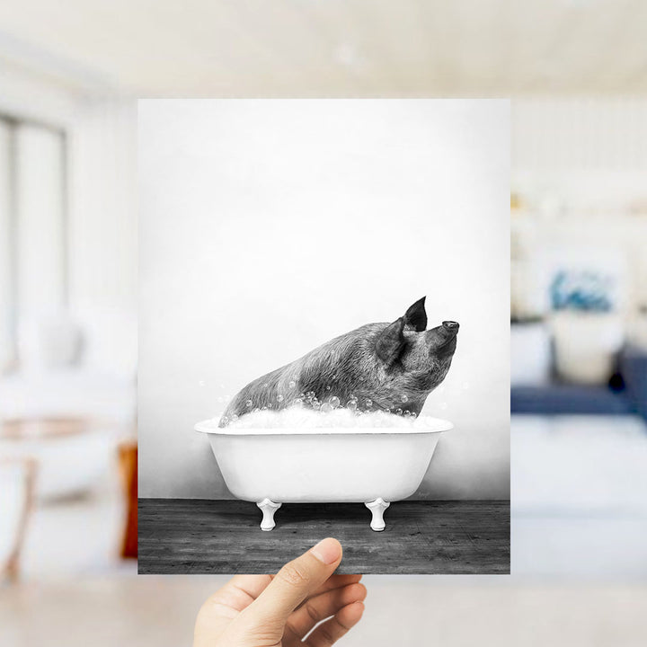 A hand holds up a black and white photograph of a pig sitting in a bathtub filled with water, creating a playful and whimsical scene.
