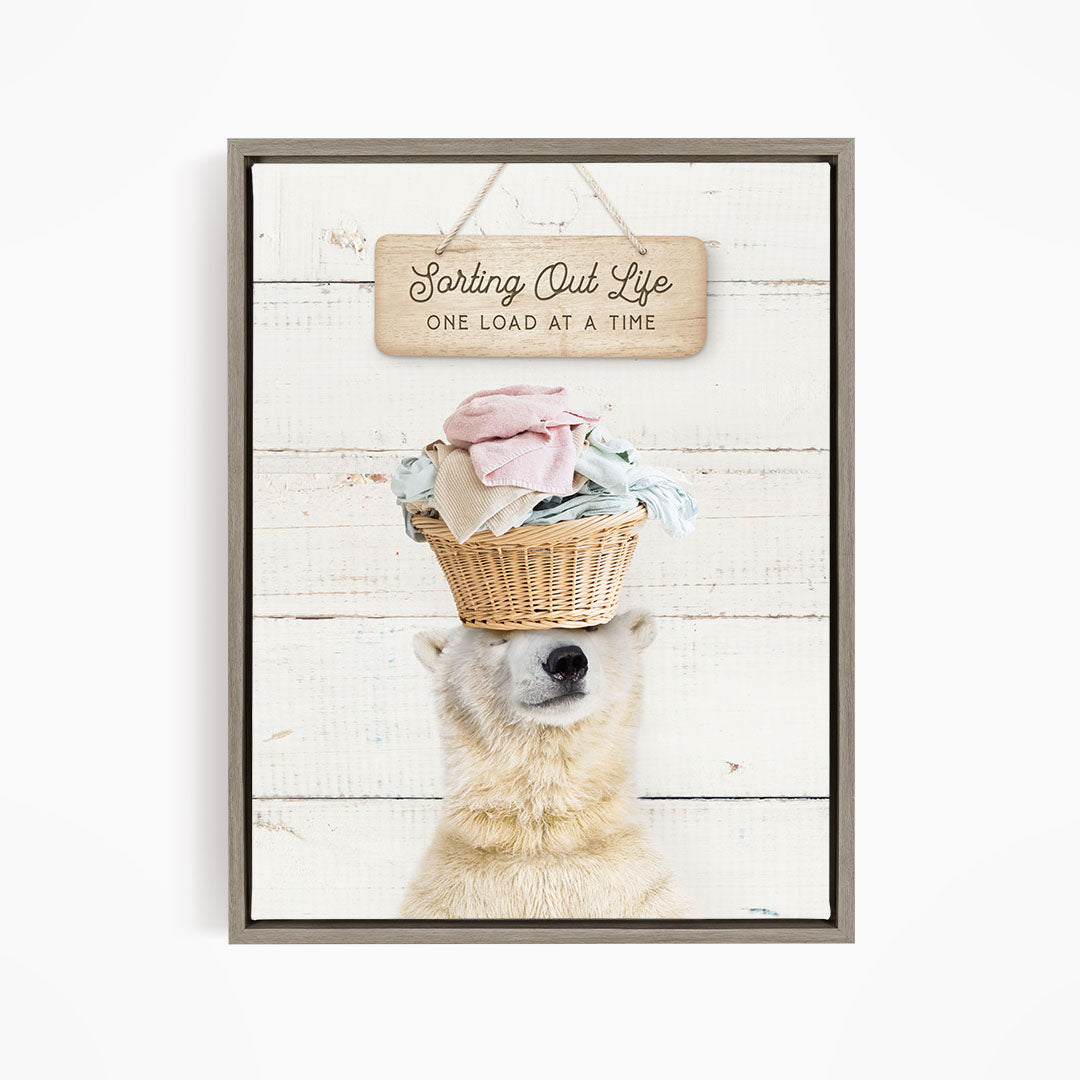 A polar bear balancing a basket of laundry on its head, with a sign above that reads "Sorting Out Life One Load at a Time".