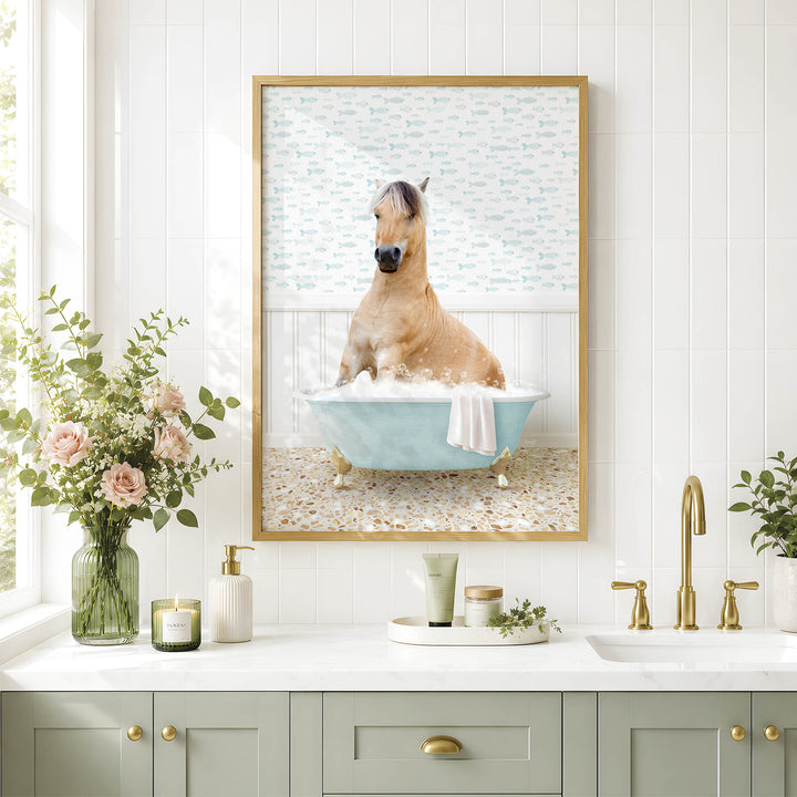 A framed image of a horse sitting in a bathtub, surrounded by flowers and a decorative vase, is displayed on a white tiled wall above a bathroom sink.