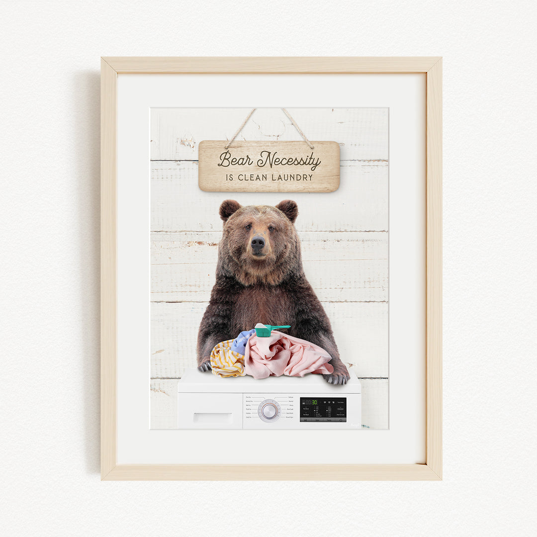 A framed image of a brown bear sitting on a washing machine, with a sign above it that says "Bear Necessity is clean laundry".