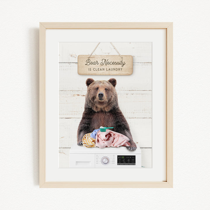 A framed image of a brown bear sitting on a washing machine, with a sign above it that says "Bear Necessity is clean laundry".
