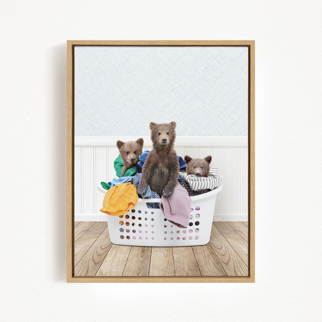 Three adorable brown bears sitting in a white laundry basket filled with clothes.