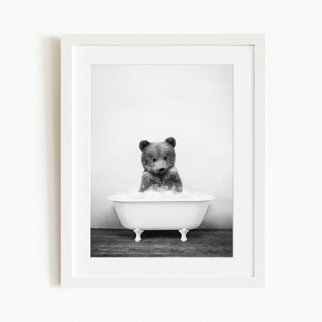 A black and white photograph of a bear sitting in a bathtub filled with water.