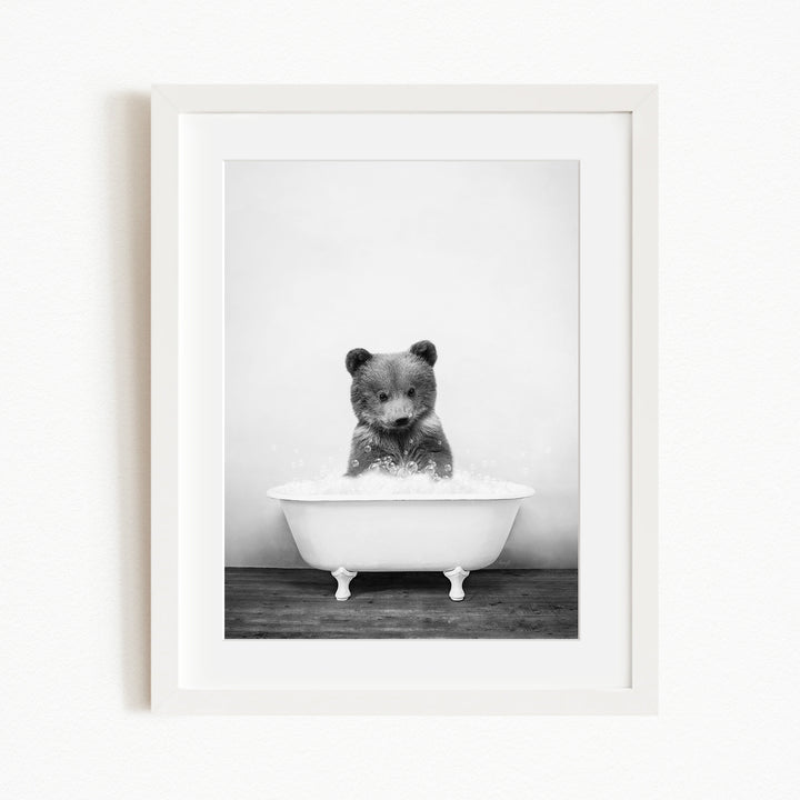 A black and white photograph of a bear sitting in a bathtub filled with water.