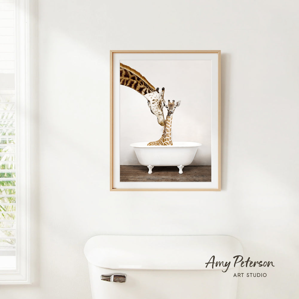 A framed image of two giraffes sitting in a white bathtub, with one giraffe extending its neck over the tub.