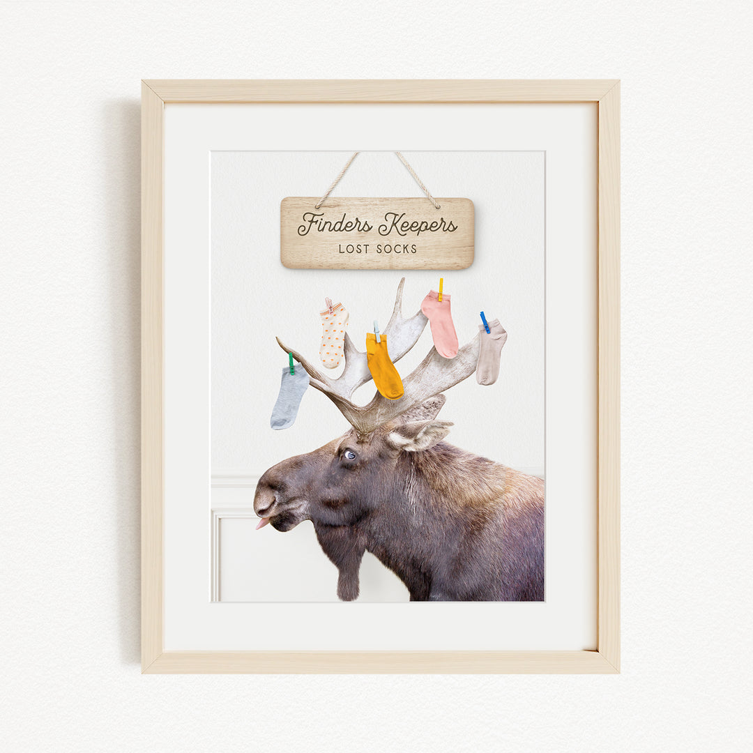 A framed image of a moose with a sign that says "Finders Keepers" hanging above it, along with a pile of colorful socks hanging from its antlers.