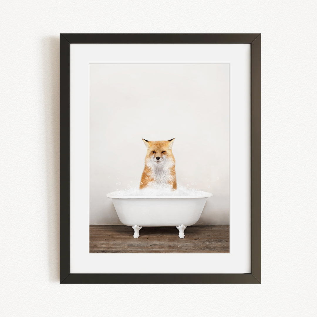 A framed image of a fox sitting in a white bathtub filled with bubbles.