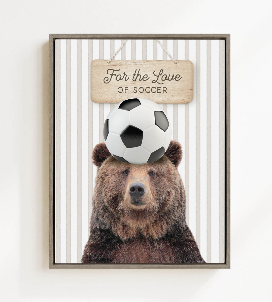 A framed image of a brown bear with a soccer ball on its head, accompanied by a wooden sign that reads "For the Love of Soccer".