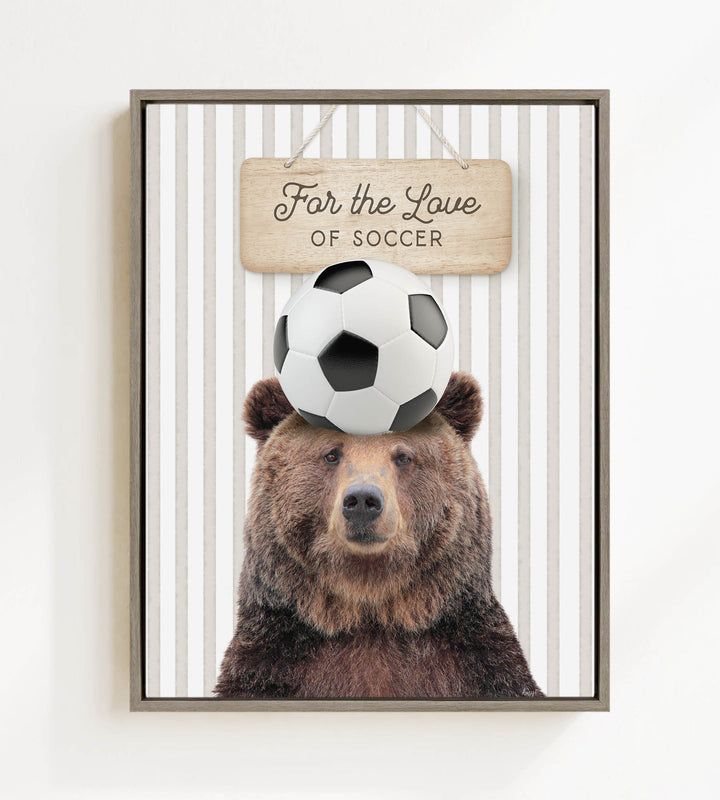 A framed image of a brown bear with a soccer ball on its head, accompanied by a wooden sign that reads "For the Love of Soccer".