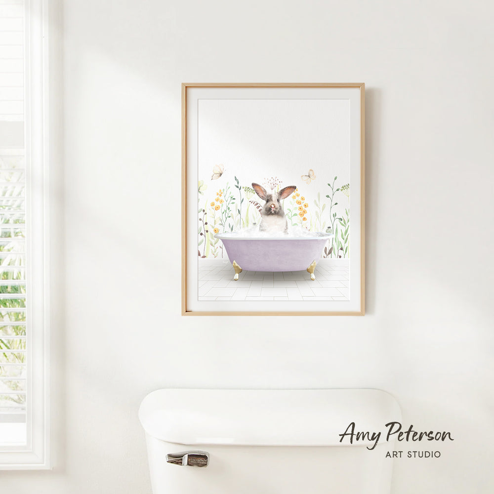 A framed illustration of a rabbit sitting in a bathtub surrounded by flowers and butterflies is hanging on a white wall.