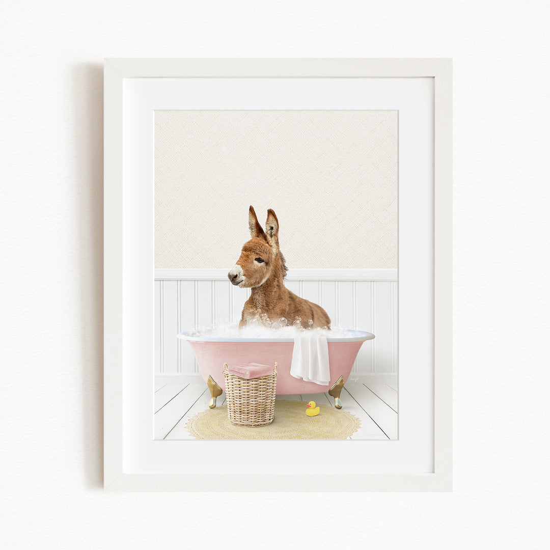 A donkey is sitting in a pink bathtub filled with water, surrounded by a yellow rubber duck and a basket.