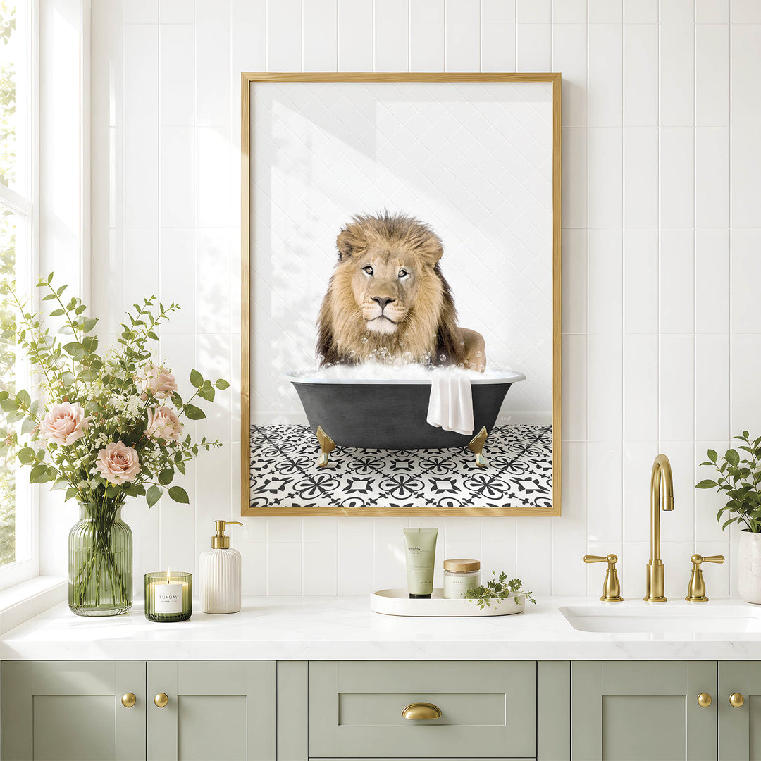 A framed image of a lion sitting in a bathtub, surrounded by flowers and candles, is displayed on a white tiled wall above a bathroom sink.