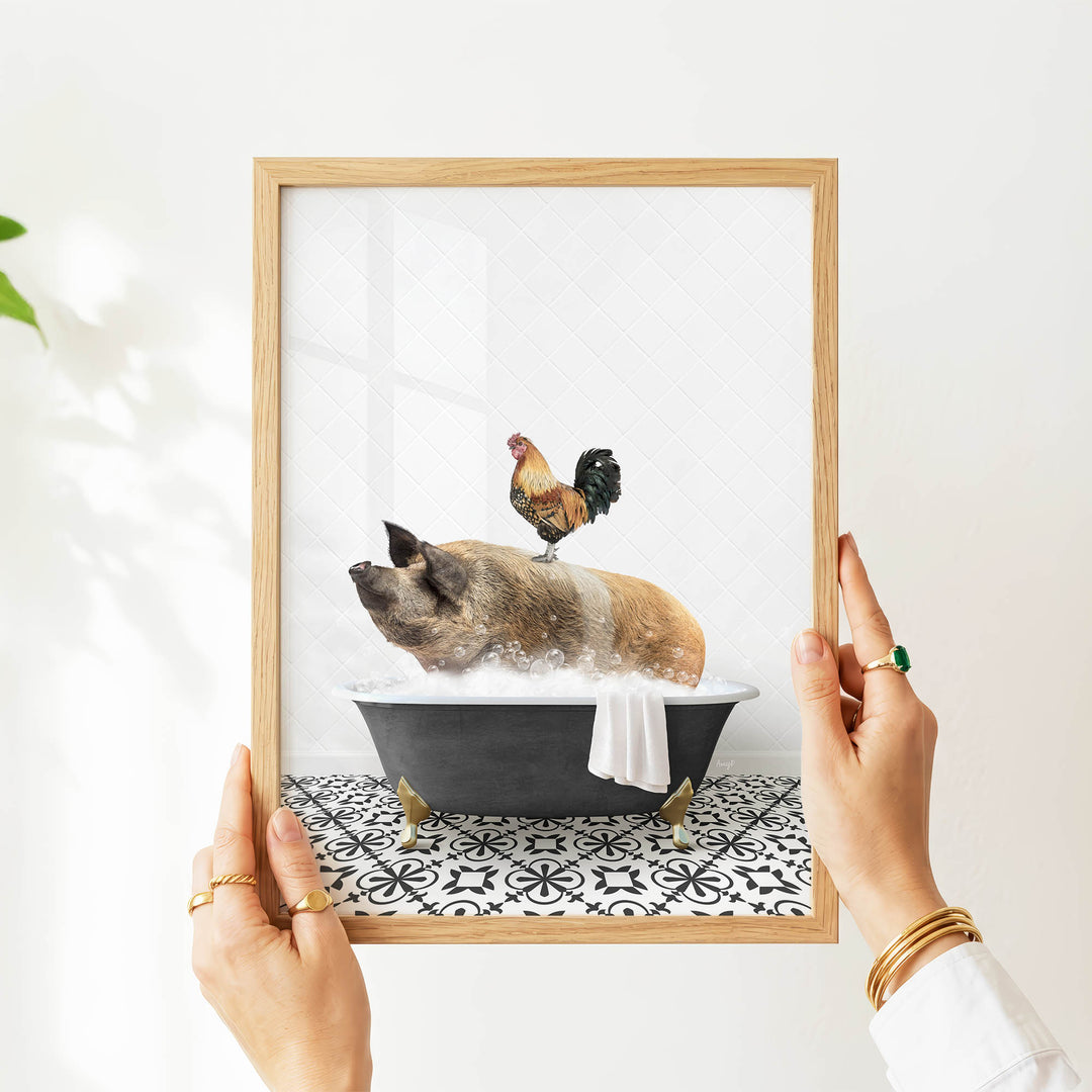 A person's hands are holding a framed image that depicts a pig sitting in a bathtub, with a rooster perched on its back.