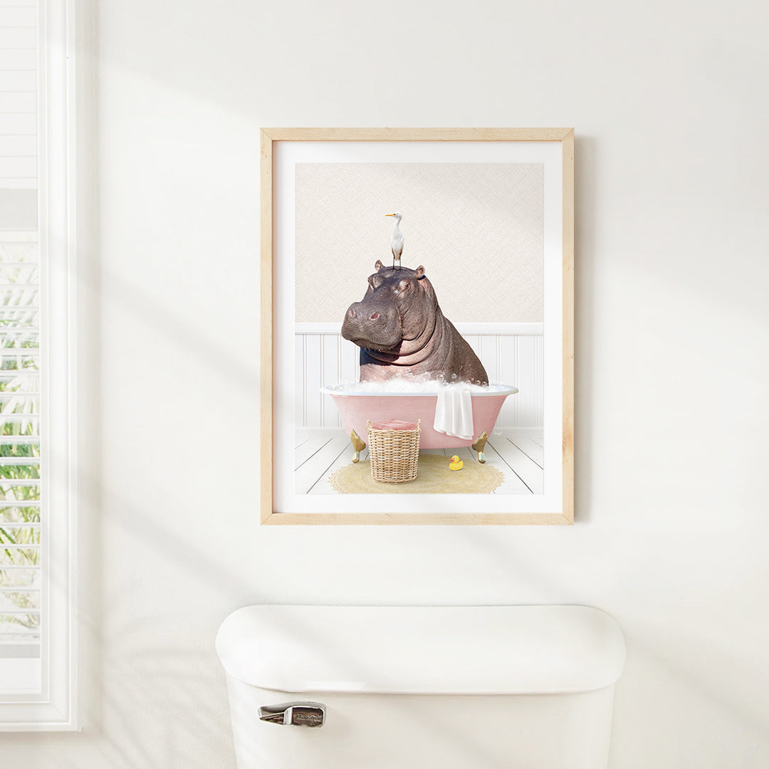 A framed image of a hippopotamus sitting in a pink bathtub, with a bird perched on its head.