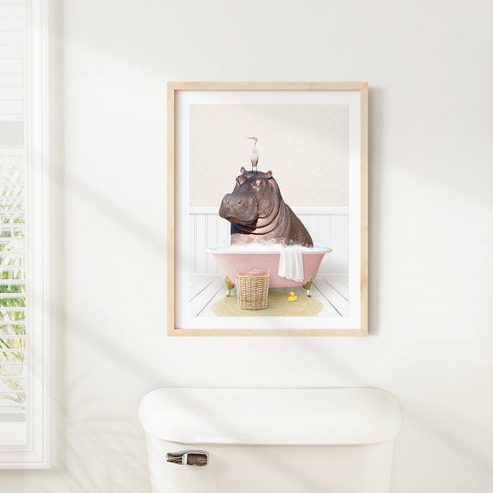 A framed image of a hippopotamus sitting in a pink bathtub, with a bird perched on its head.
