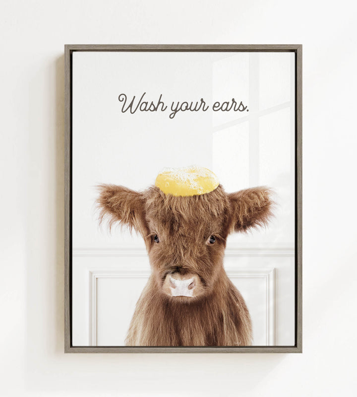 A framed image of a brown cow with a yellow object on its head, accompanied by the text "Wash your ears."