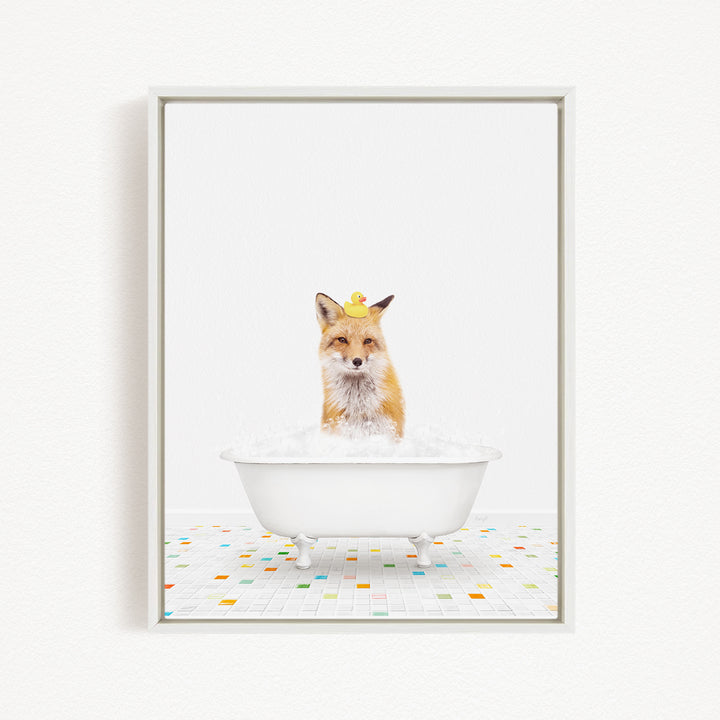 A fox is sitting in a white bathtub filled with bubbles, with a yellow rubber duck perched on its head.