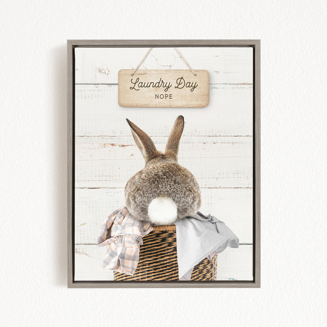 A wooden sign with the text "Laundry Day Hope" hangs above a basket containing a plaid blanket and a white rabbit.