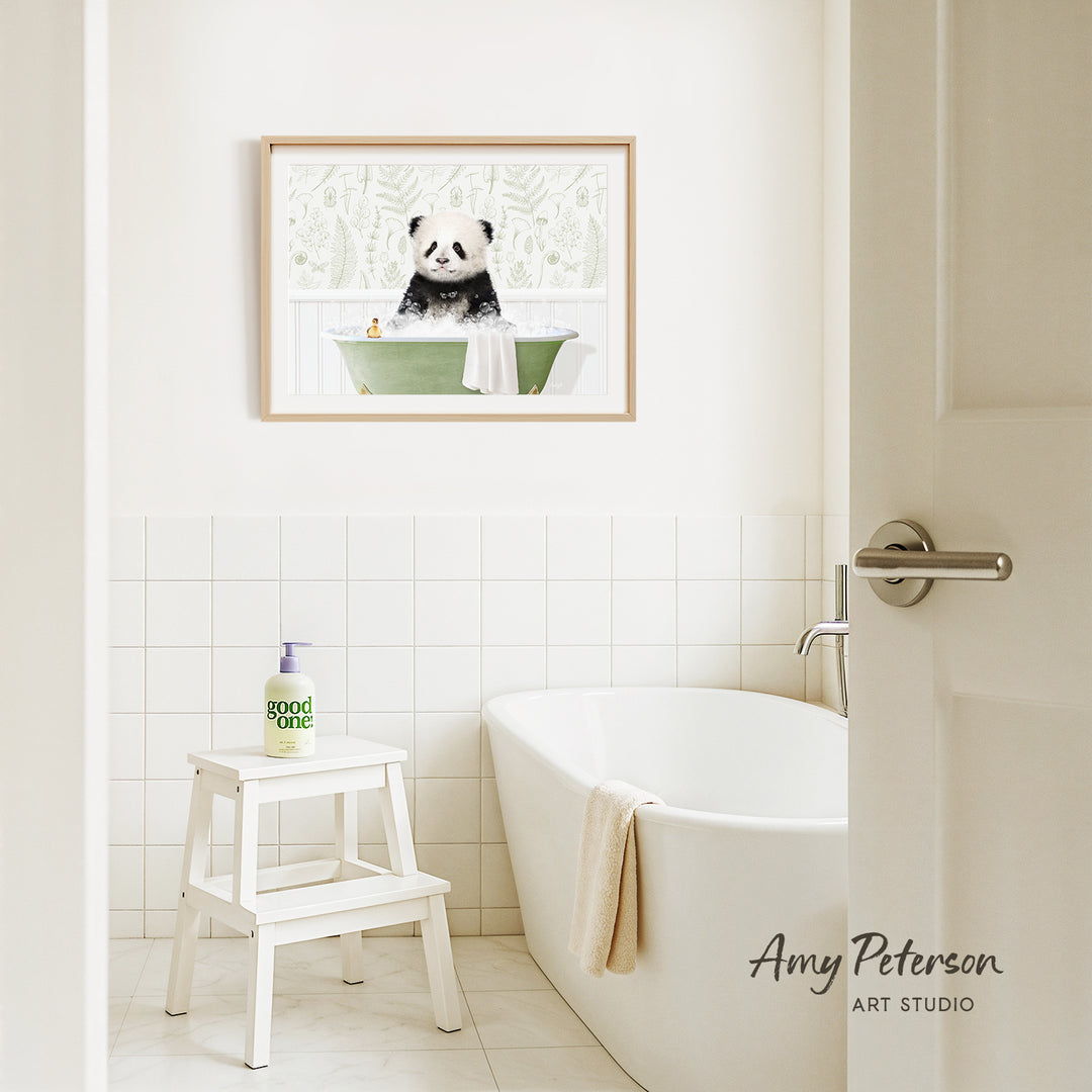A framed image of a panda sitting in a bathtub is hanging on a white tiled wall above a white bathtub in a bathroom.
