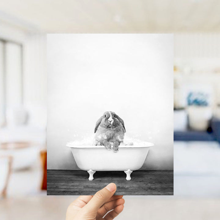 A hand holds up a black and white photograph of a rabbit sitting in a bathtub filled with bubbles.