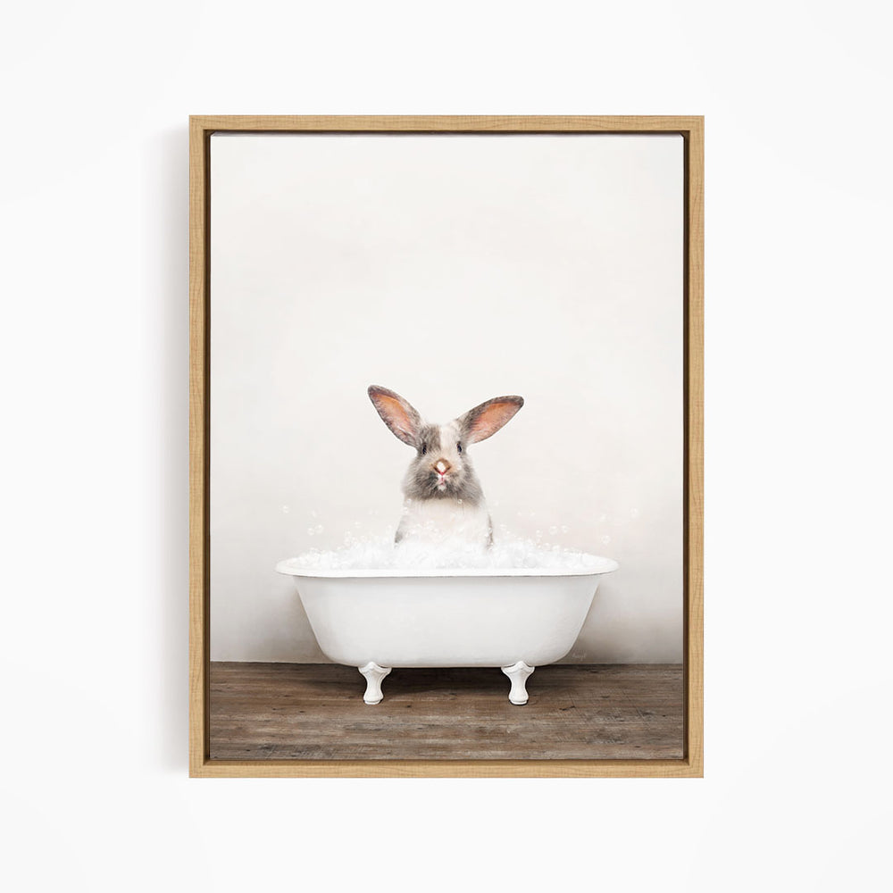 A white rabbit sitting in a white bathtub filled with bubbles, looking directly at the camera.