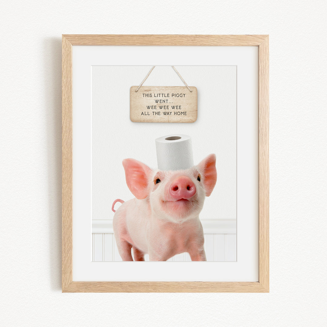 A framed image of a pig with a sign above it that reads "This little piggy went to the bathroom. Wee wee wee all the way home."