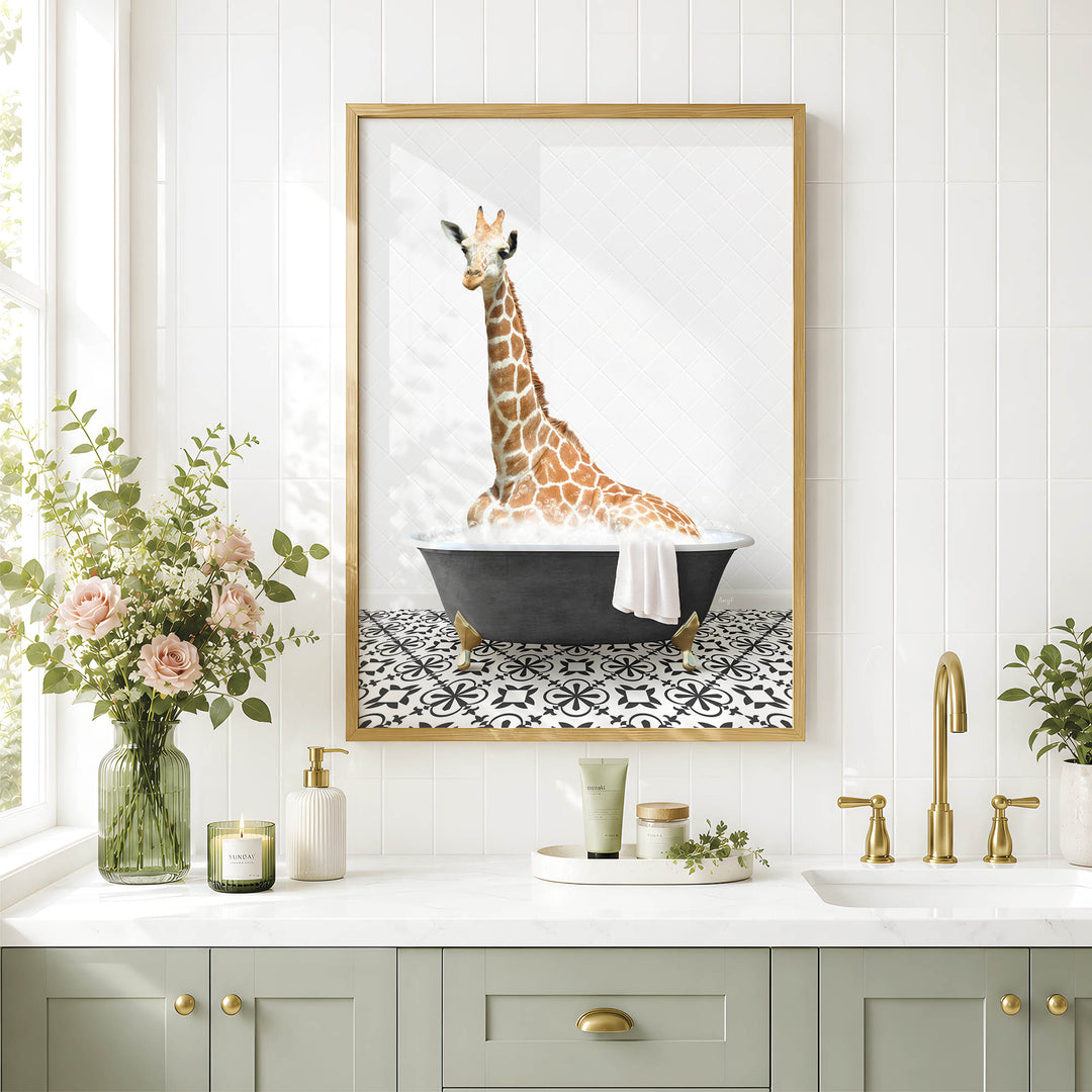 A framed image of a giraffe sitting in a bathtub is displayed on a white tiled wall above a bathroom counter with various toiletries and a vase of flowers.