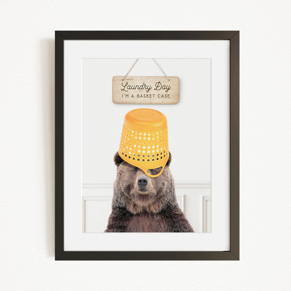 A framed image of a bear wearing a yellow laundry basket on its head, with a sign above that says "Laundry Day I'm a basket case".