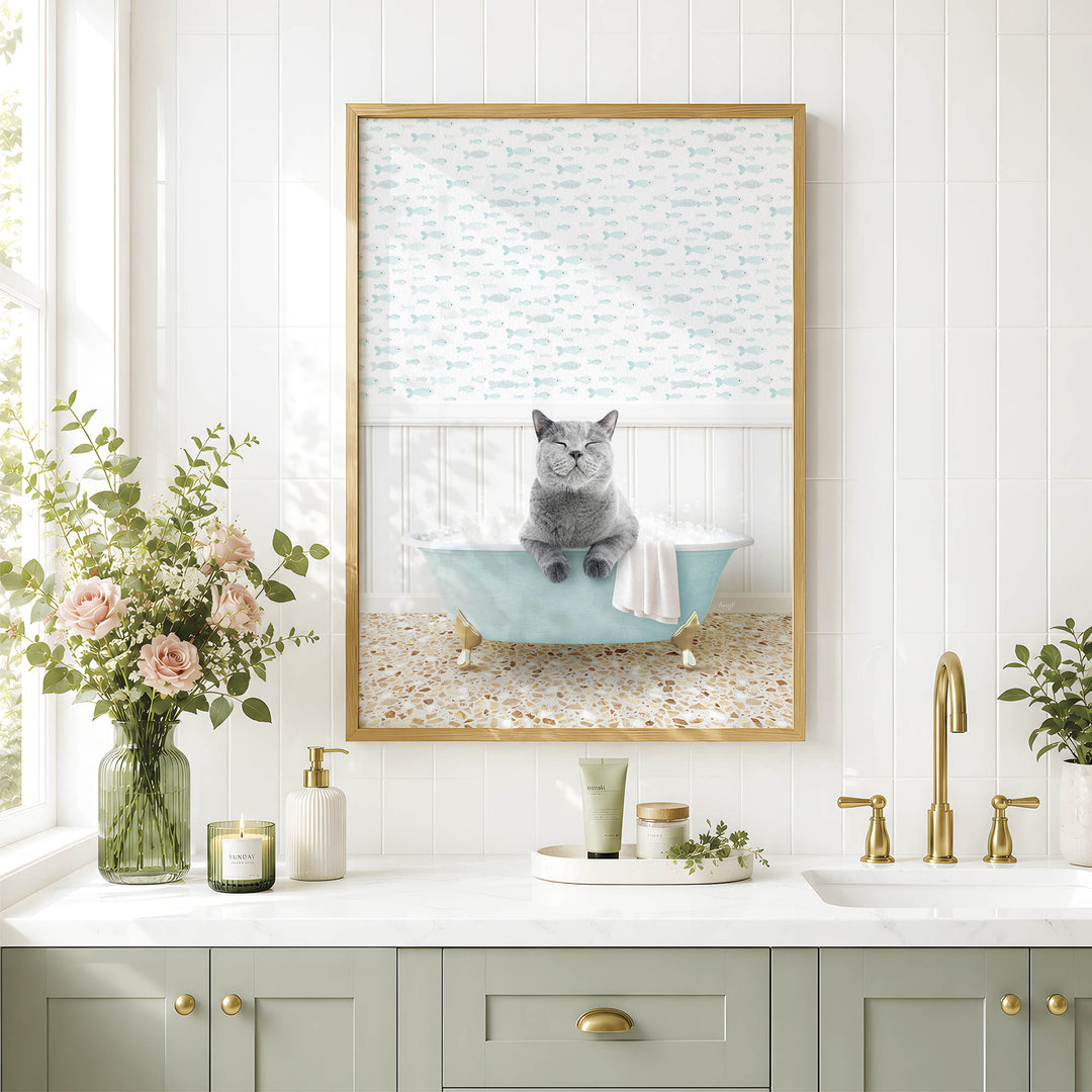 A framed image of a gray cat sitting in a blue bathtub, surrounded by flowers and a green vase, is displayed on a white tiled wall above a bathroom sink.