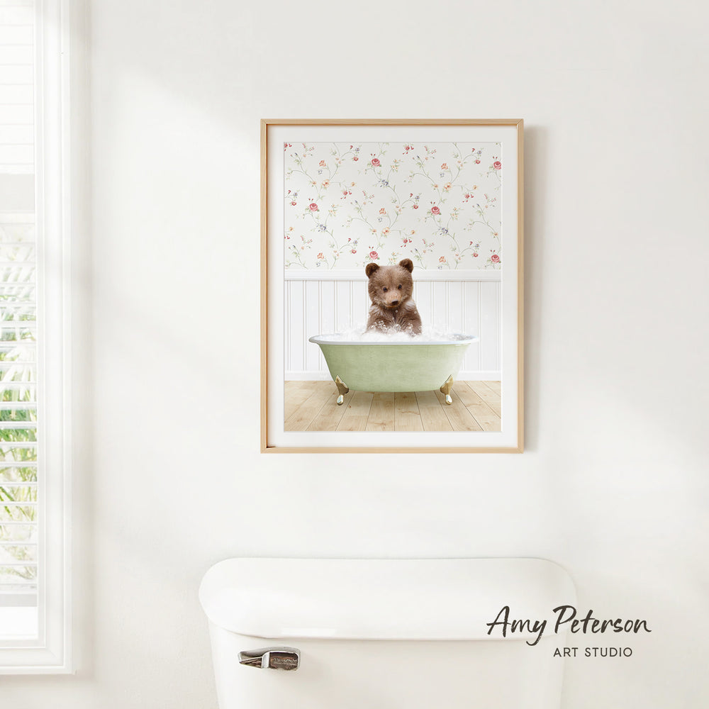 A framed image of a brown bear sitting in a green bathtub, with a floral pattern on the wall behind it.