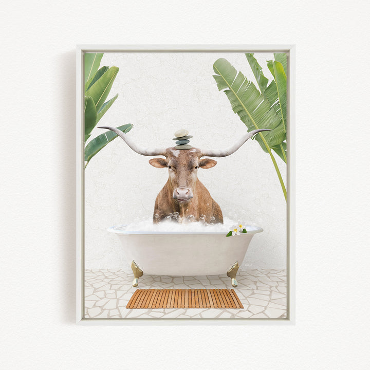 A brown cow with large horns is sitting in a white bathtub filled with water, surrounded by green leaves and a wooden mat on the floor.