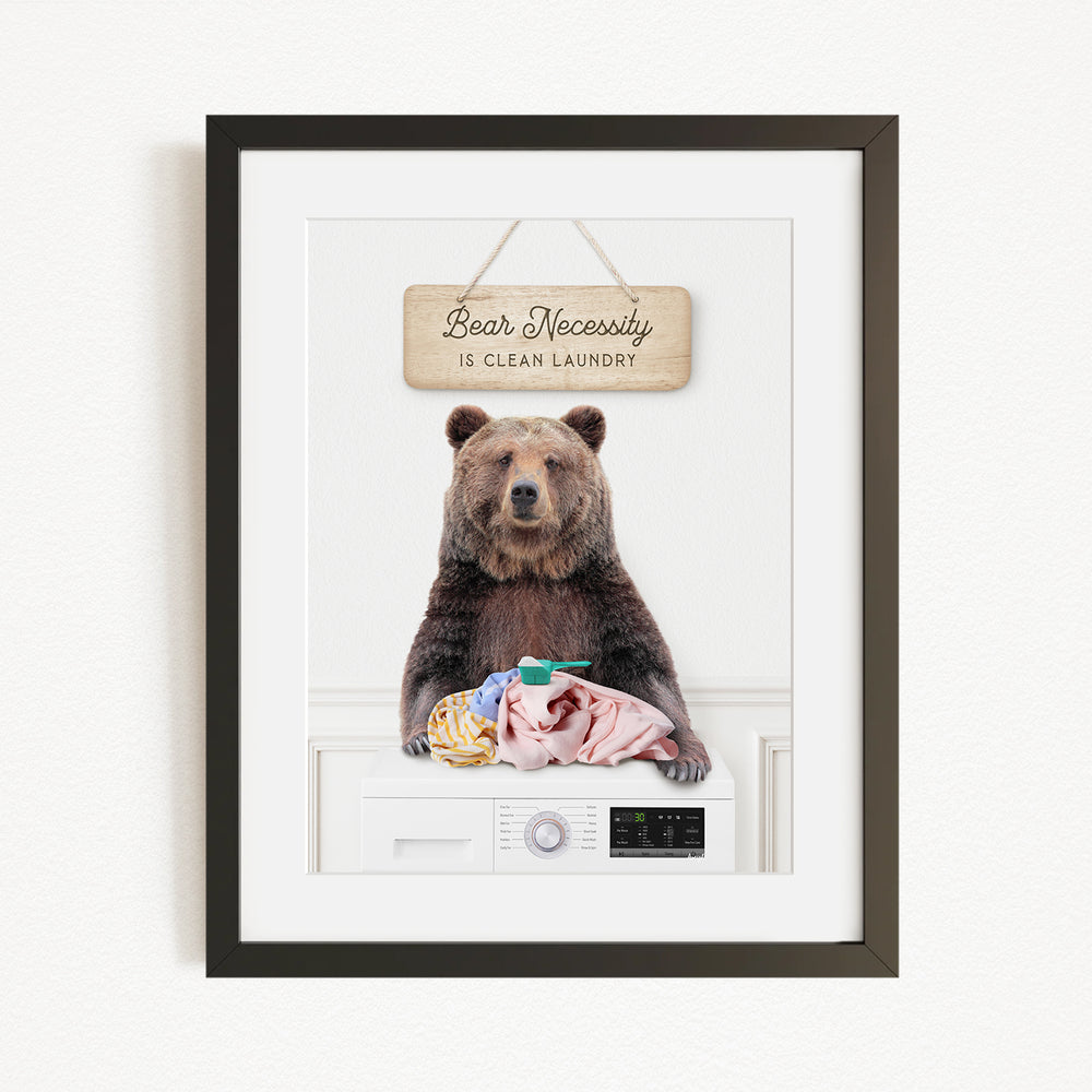 A framed image of a brown bear sitting on a washing machine, with a sign above that says "Bear Necessity is clean laundry".