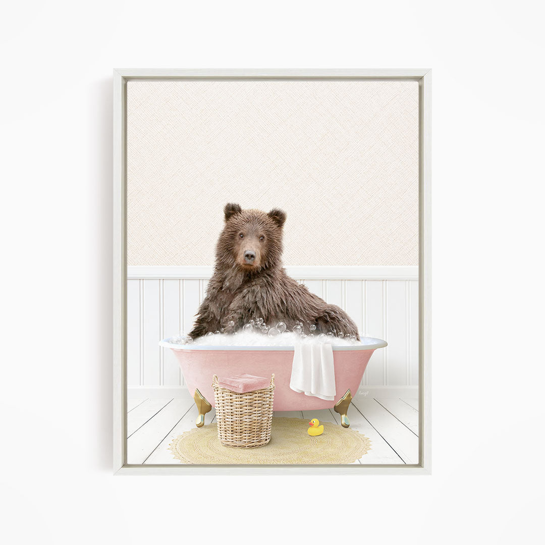 A brown bear sitting in a pink bathtub filled with bubbles, surrounded by a yellow rubber duck and a wicker basket.