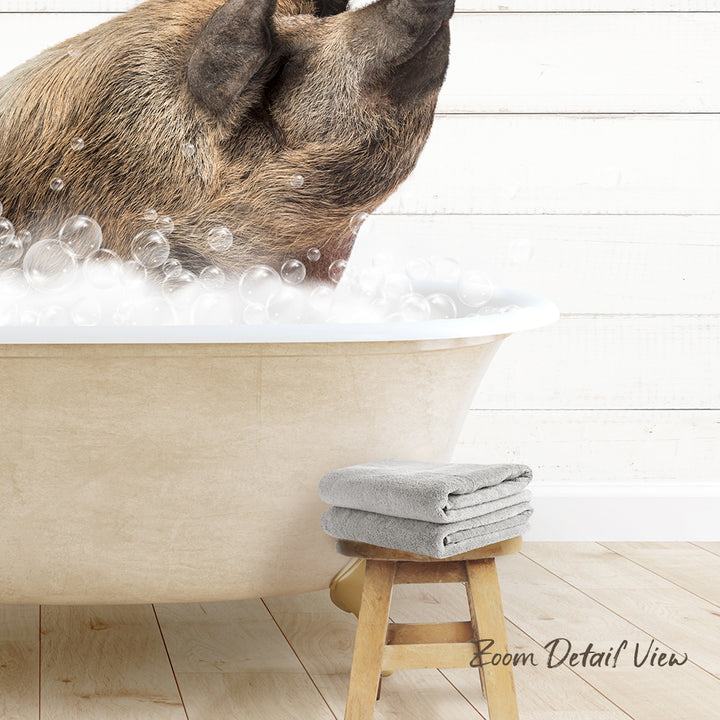A dog is sitting in a bathtub filled with bubbles, with a towel and stool nearby.