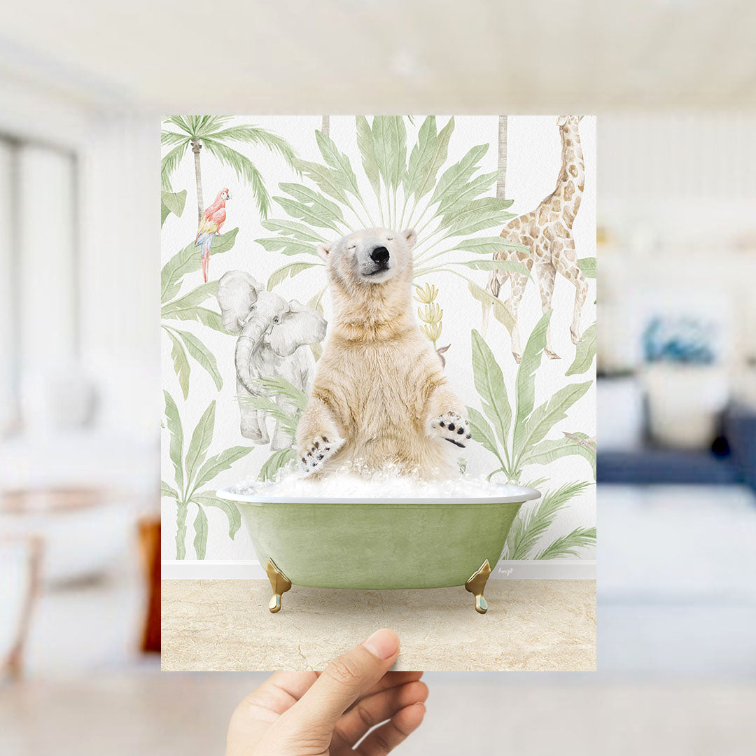 A hand holds up a framed print featuring a polar bear sitting in a bathtub surrounded by tropical plants and animals, including a giraffe and a parrot.