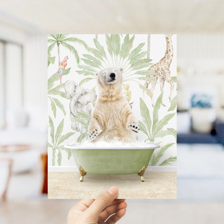 A hand holds up a framed print featuring a polar bear sitting in a bathtub surrounded by tropical plants and animals, including a giraffe and a parrot.