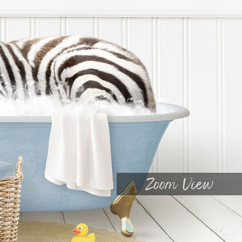 A zebra lying in a blue bathtub filled with bubbles, surrounded by a yellow rubber duck and a towel.