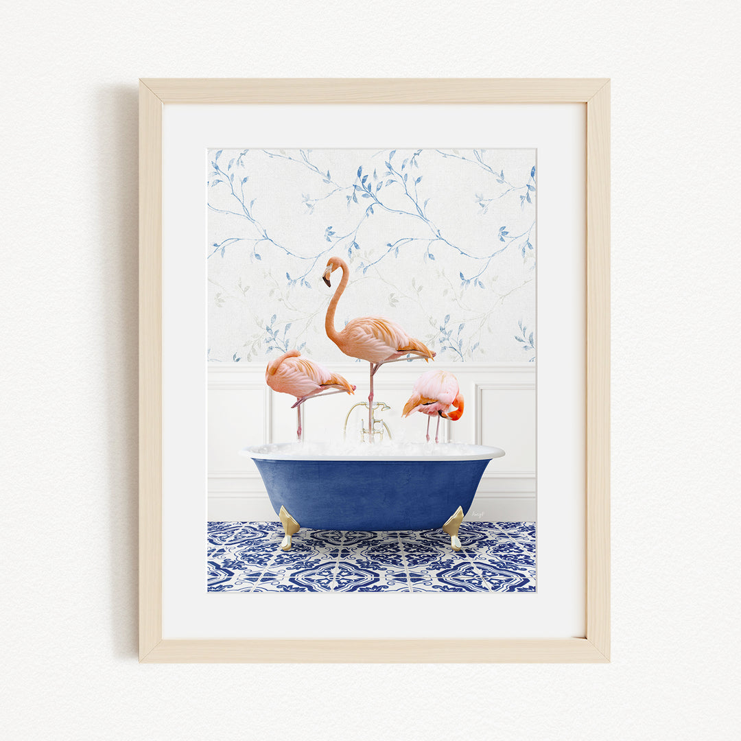 A framed image depicting three flamingos standing in a blue bathtub, with a patterned tile floor and a floral wallpaper in the background.