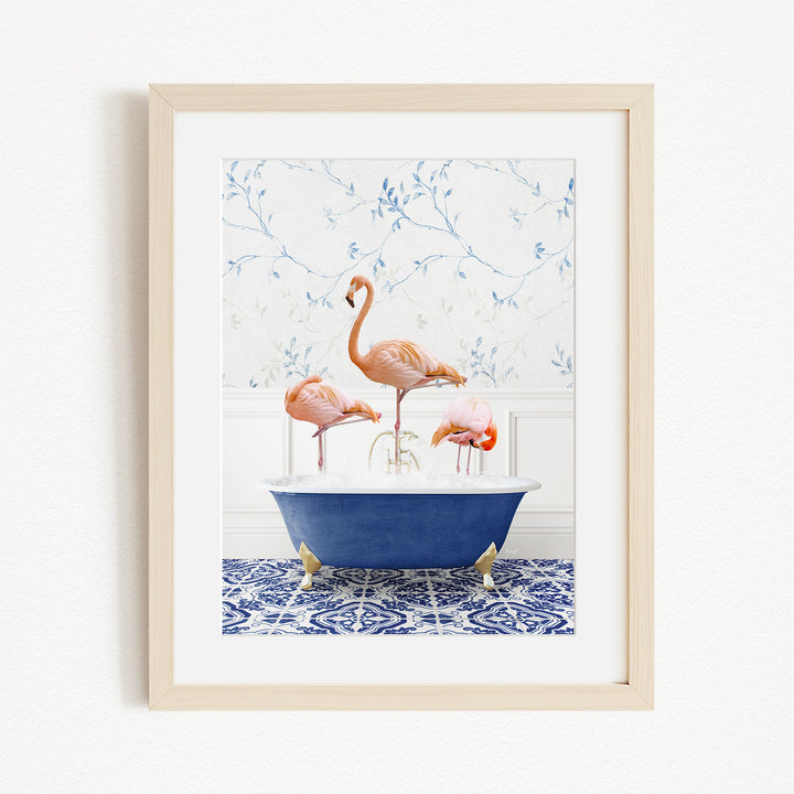 A framed image depicting three flamingos standing in a blue bathtub, with a patterned tile floor and a floral wallpaper in the background.