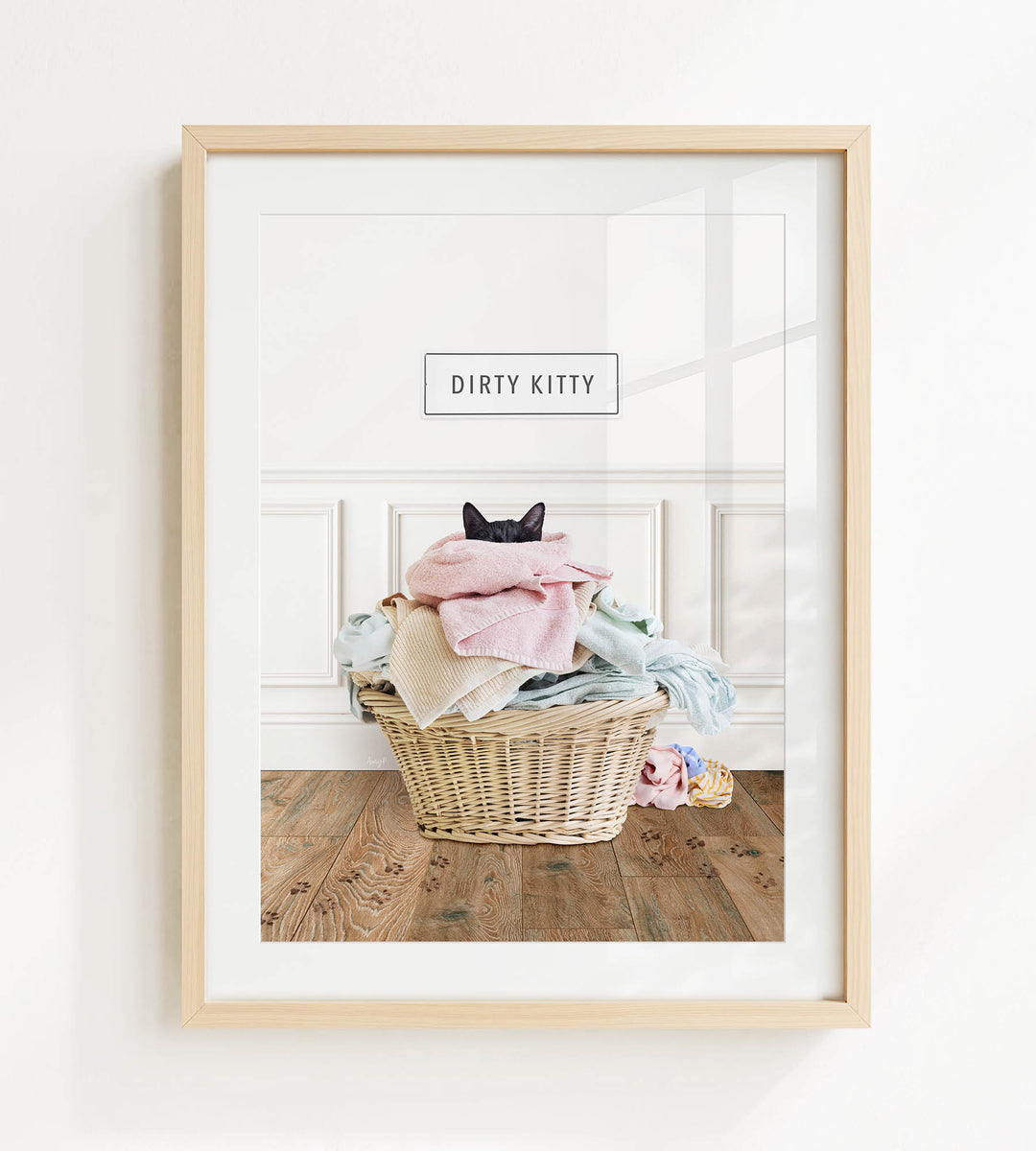 A framed image of a cat sitting in a basket filled with clothes, with the text "Dirty Kitty" displayed above the basket.