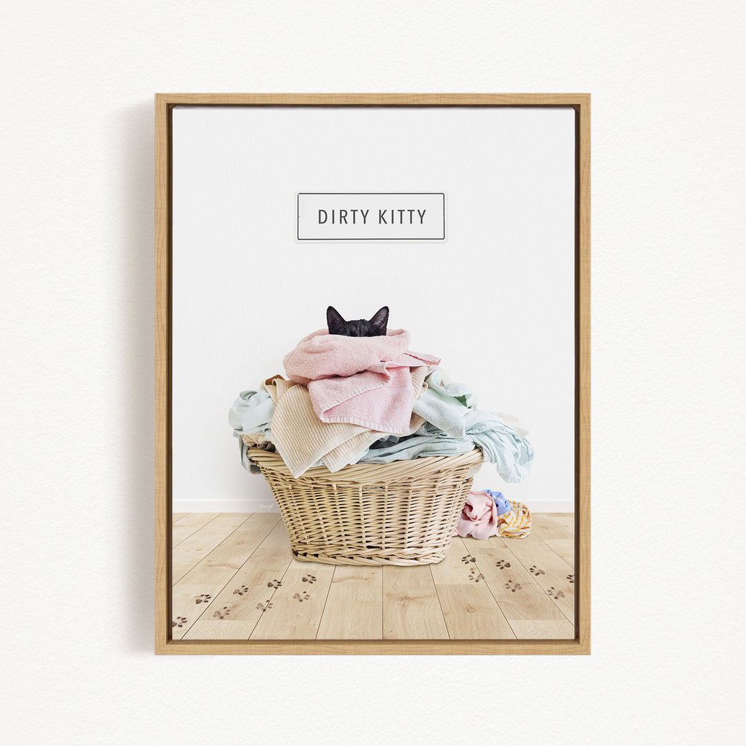 A framed image depicting a cat sitting in a basket filled with clothes, with the text "Dirty Kitty" displayed above the basket.