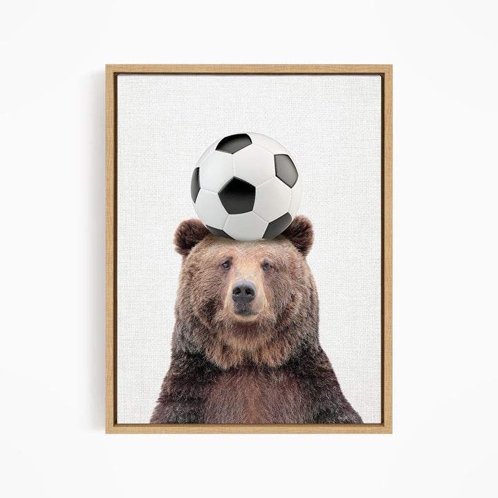 A brown bear balancing a soccer ball on its head.