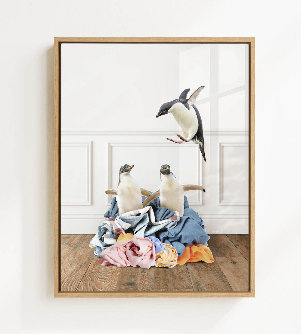 A framed image depicting two penguins sitting on a pile of clothes, with one penguin flying in the background.